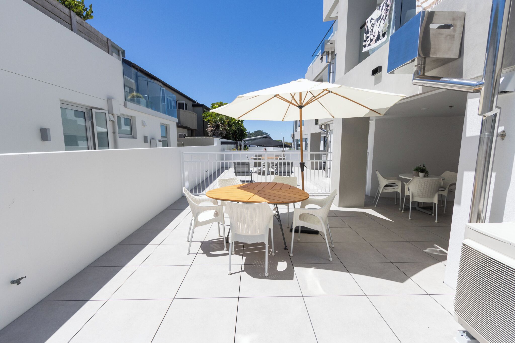 A patio with a round table, white chairs, and a large umbrella.