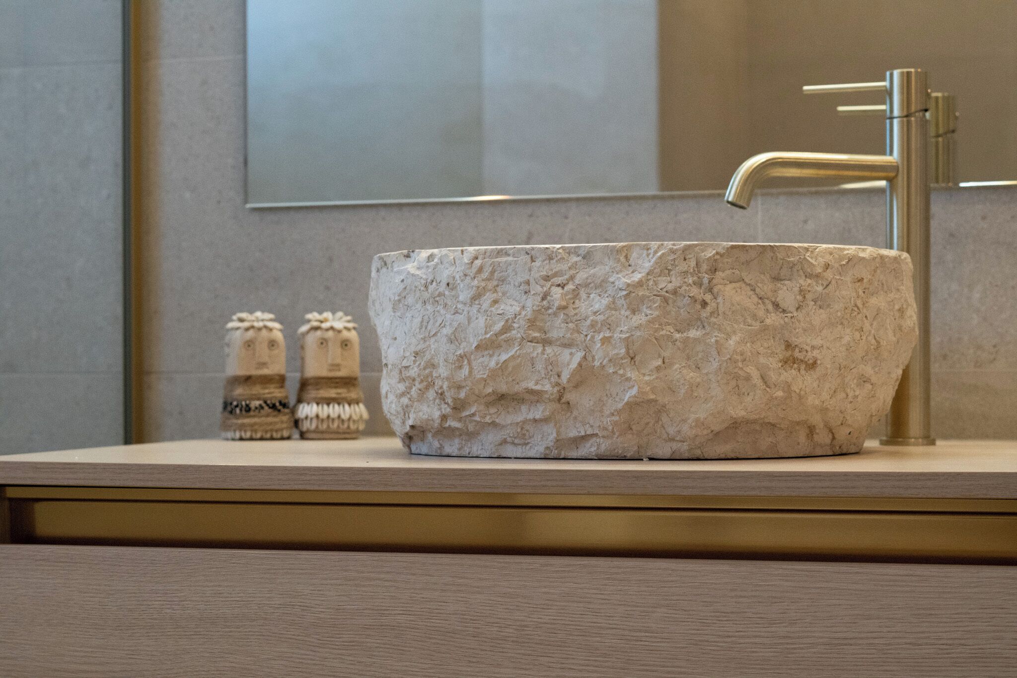 A bathroom with a large, natural stone sink, a modern faucet, and two salt and pepper shakers on the counter.