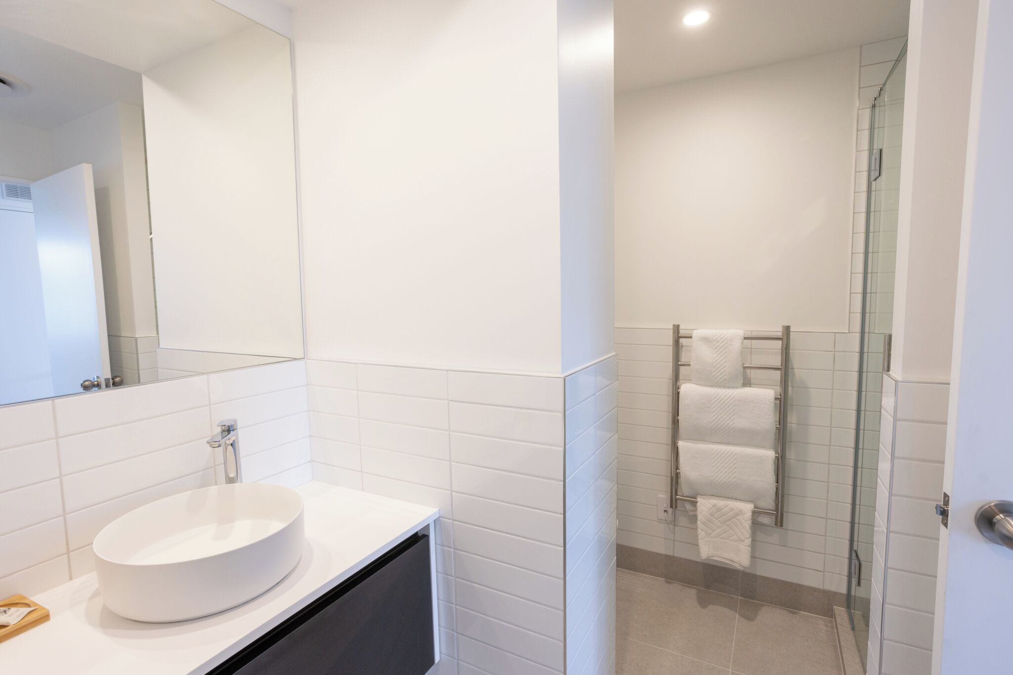 A modern bathroom with a round white sink, a glass shower enclosure, and a mirror above the sink.