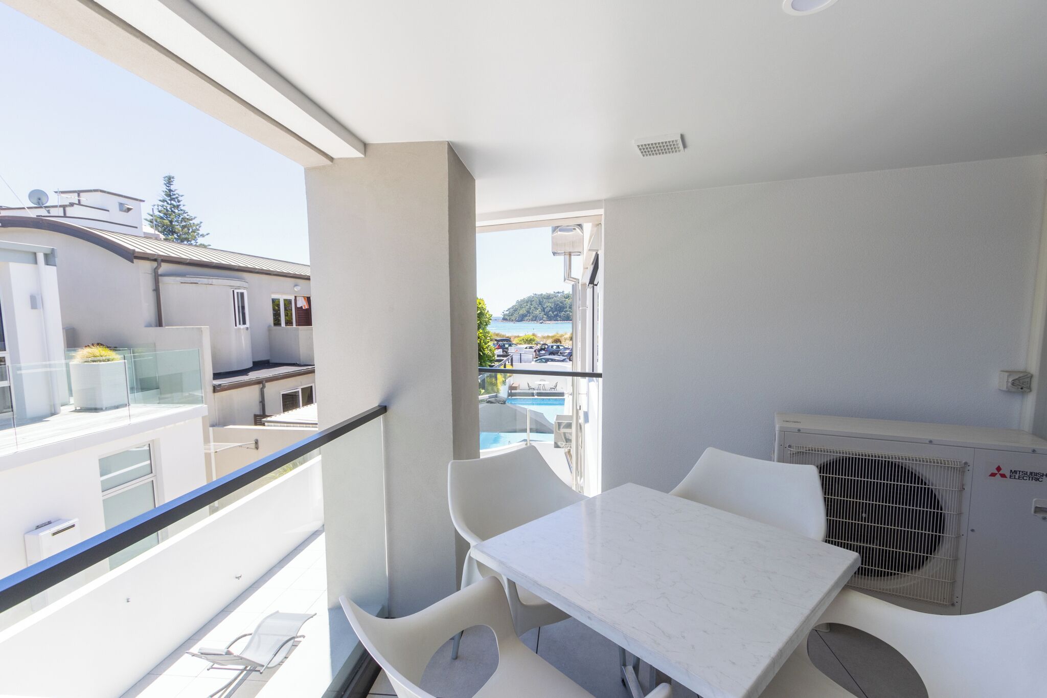 Varanda com mesa e cadeiras, piscina ao fundo e um aparelho de ar condicionado.