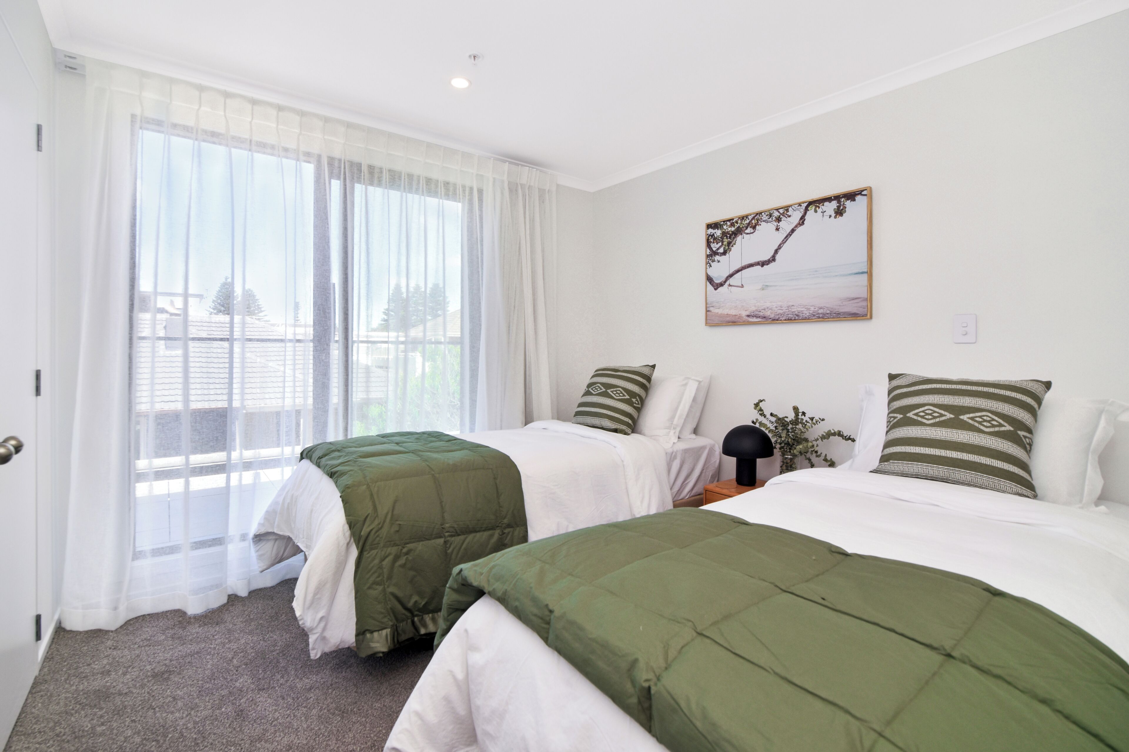 Habitación de hotel con dos camas, un ventanal con cortinas translúcidas, un cuadro en la pared y vistas al exterior.