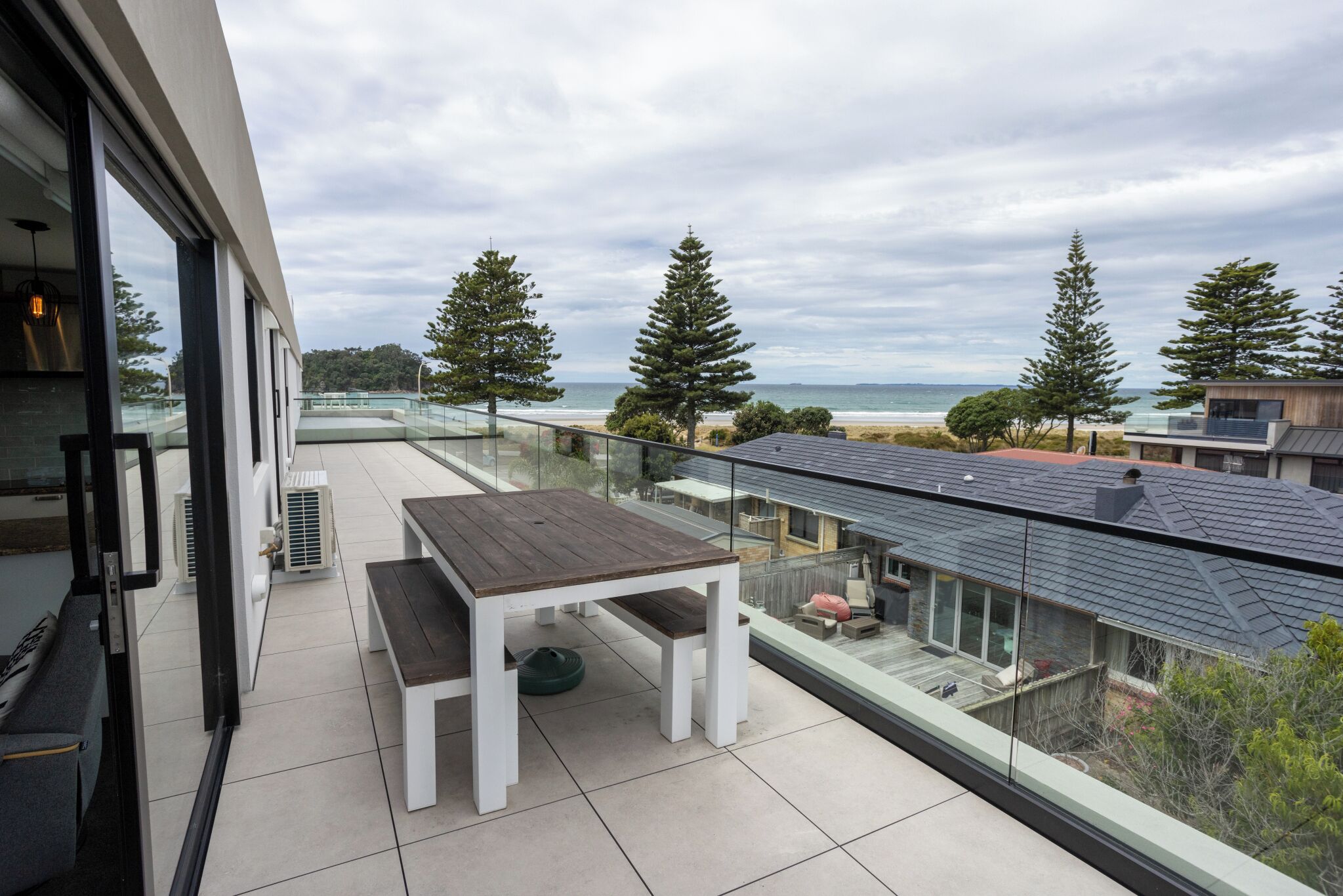 Ein Balkon mit Holztisch und Bänken mit Blick auf Strand und Meer.