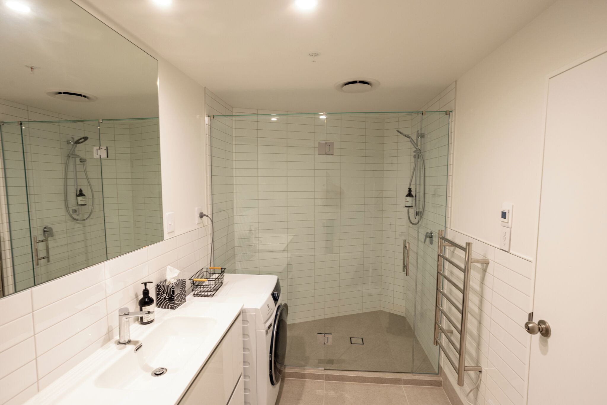 A modern bathroom with a glass-enclosed shower, a large mirror, and a white sink with a towel rack.