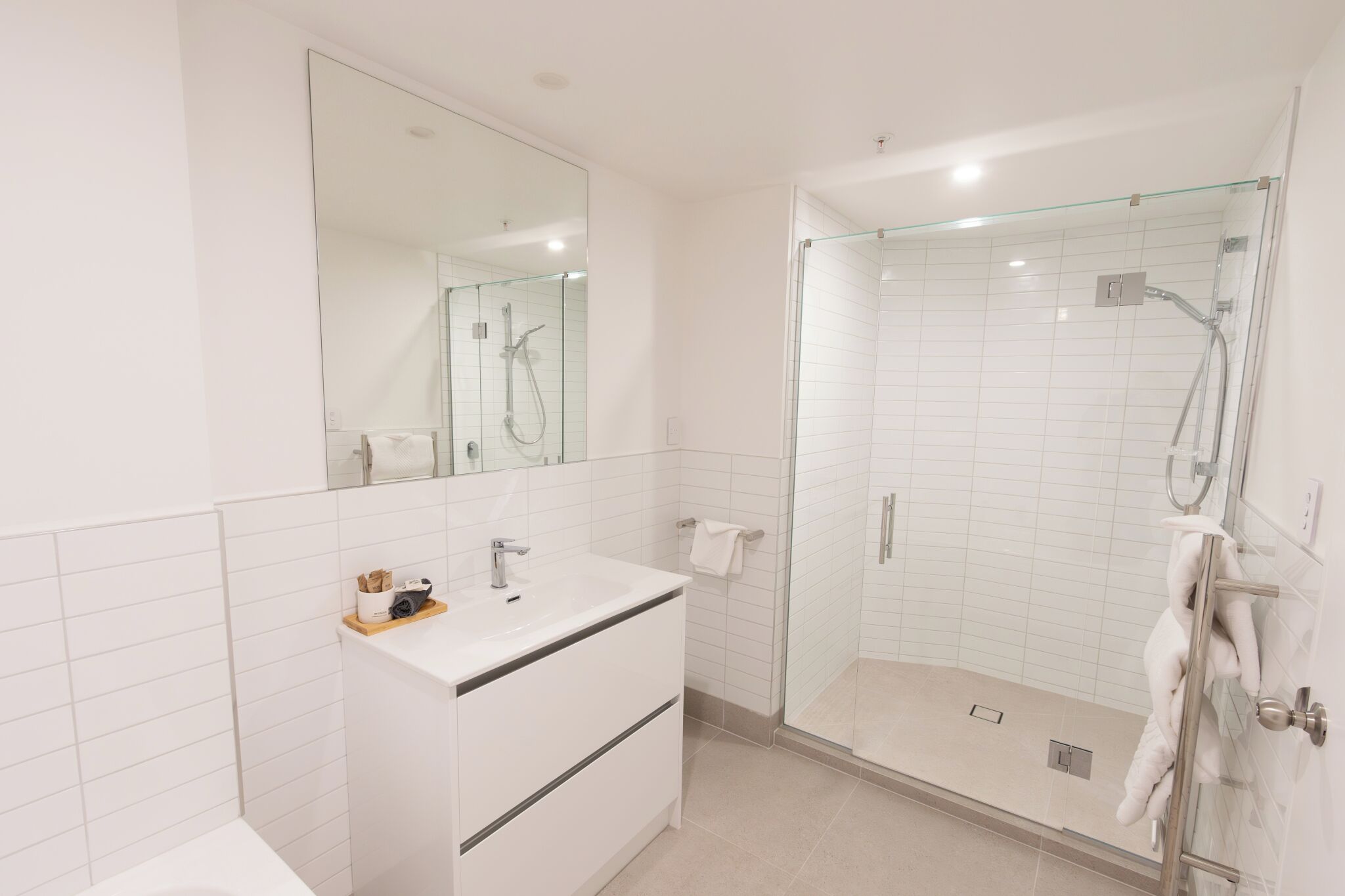 A modern bathroom with a glass-enclosed shower, a white sink, and a large mirror.