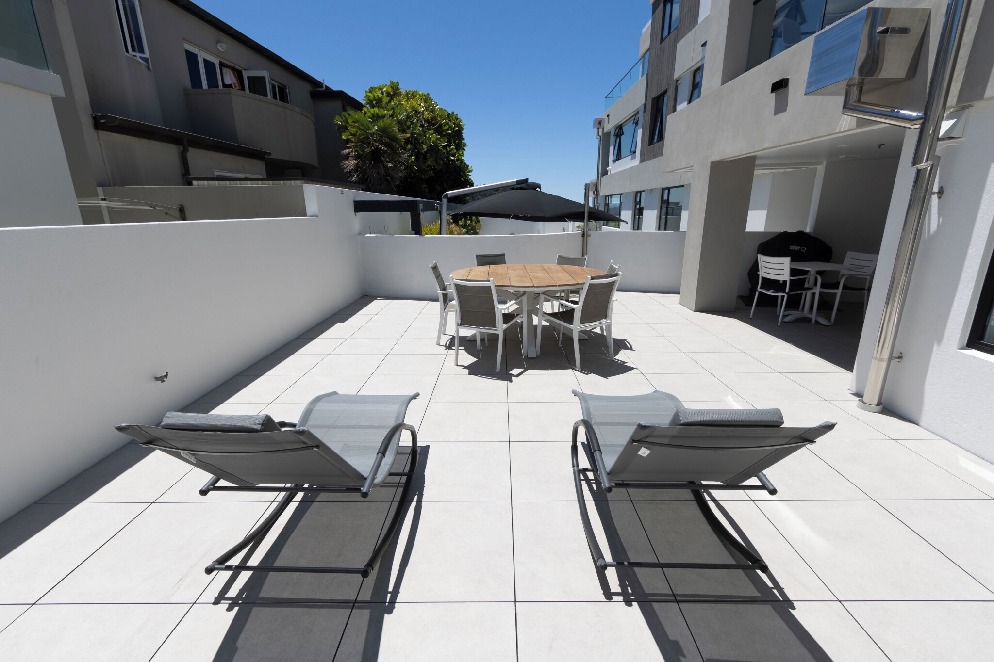 Un patio en la azotea con una mesa redonda y sillas, una parrilla y sillones de relax.