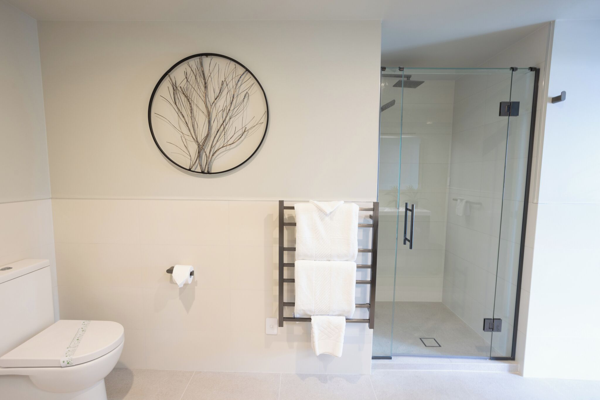 Et moderne badeværelse med toilet, glasbrusekabine og håndklædetørrestativ.