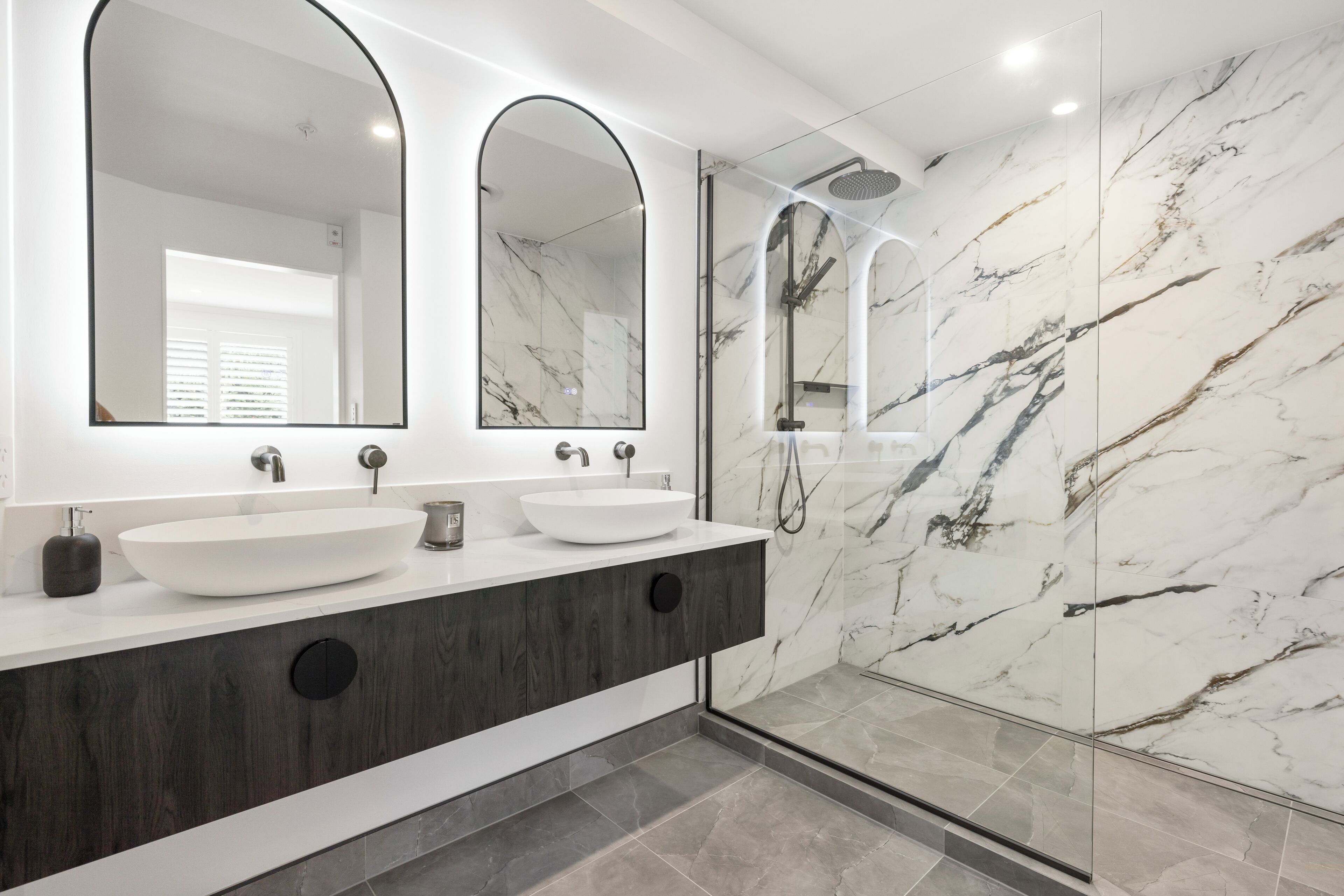 A modern bathroom with a white vanity, two large mirrors, a white sink, and a glass-enclosed shower area.