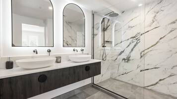 A modern bathroom with a white vanity, two large mirrors, a white sink, and a glass-enclosed shower area.