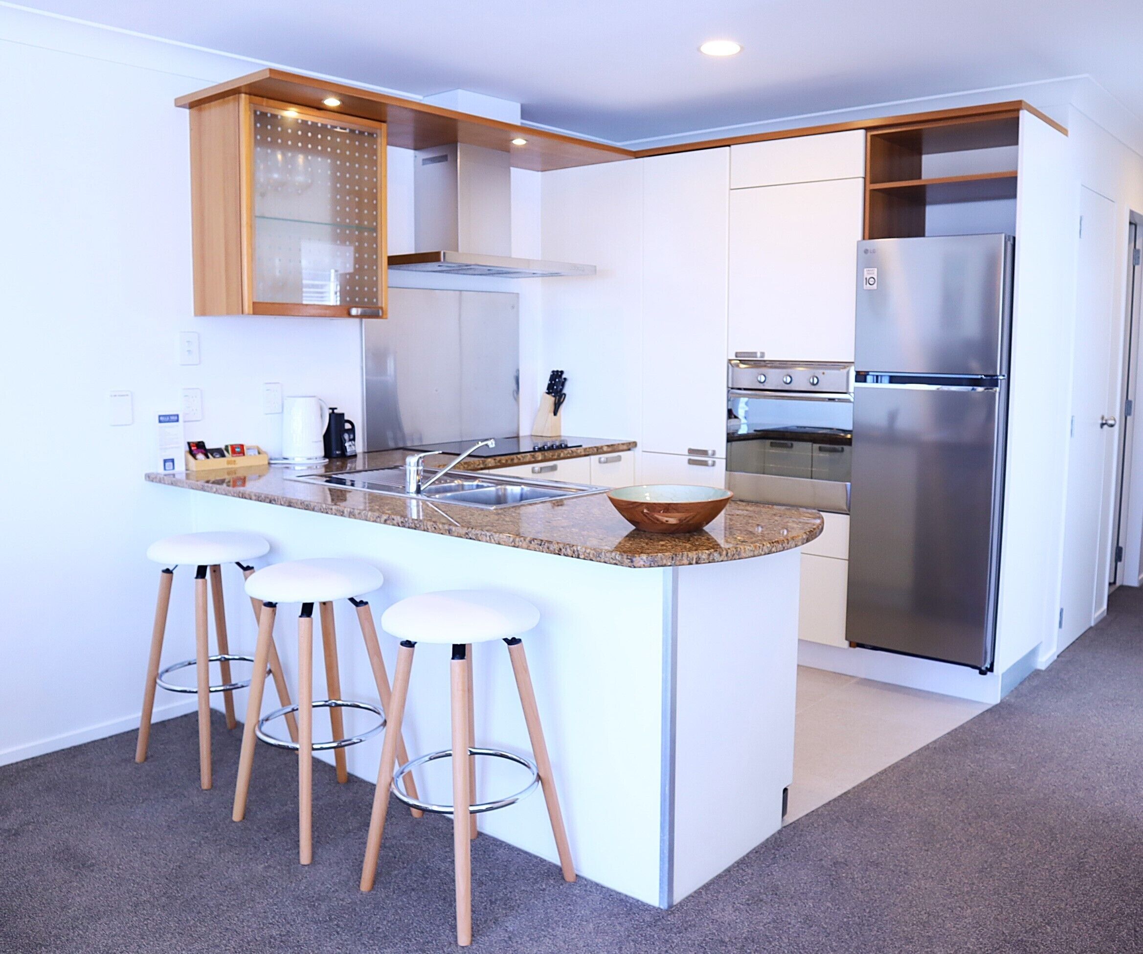 Une cuisine moderne dotée d’un îlot central, de tabourets de bar, d’appareils électroménagers en acier inoxydable et de meubles de rangement blancs.