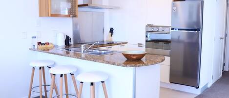Une cuisine moderne dotée d’un îlot central, de tabourets de bar, d’appareils électroménagers en acier inoxydable et de meubles de rangement blancs.