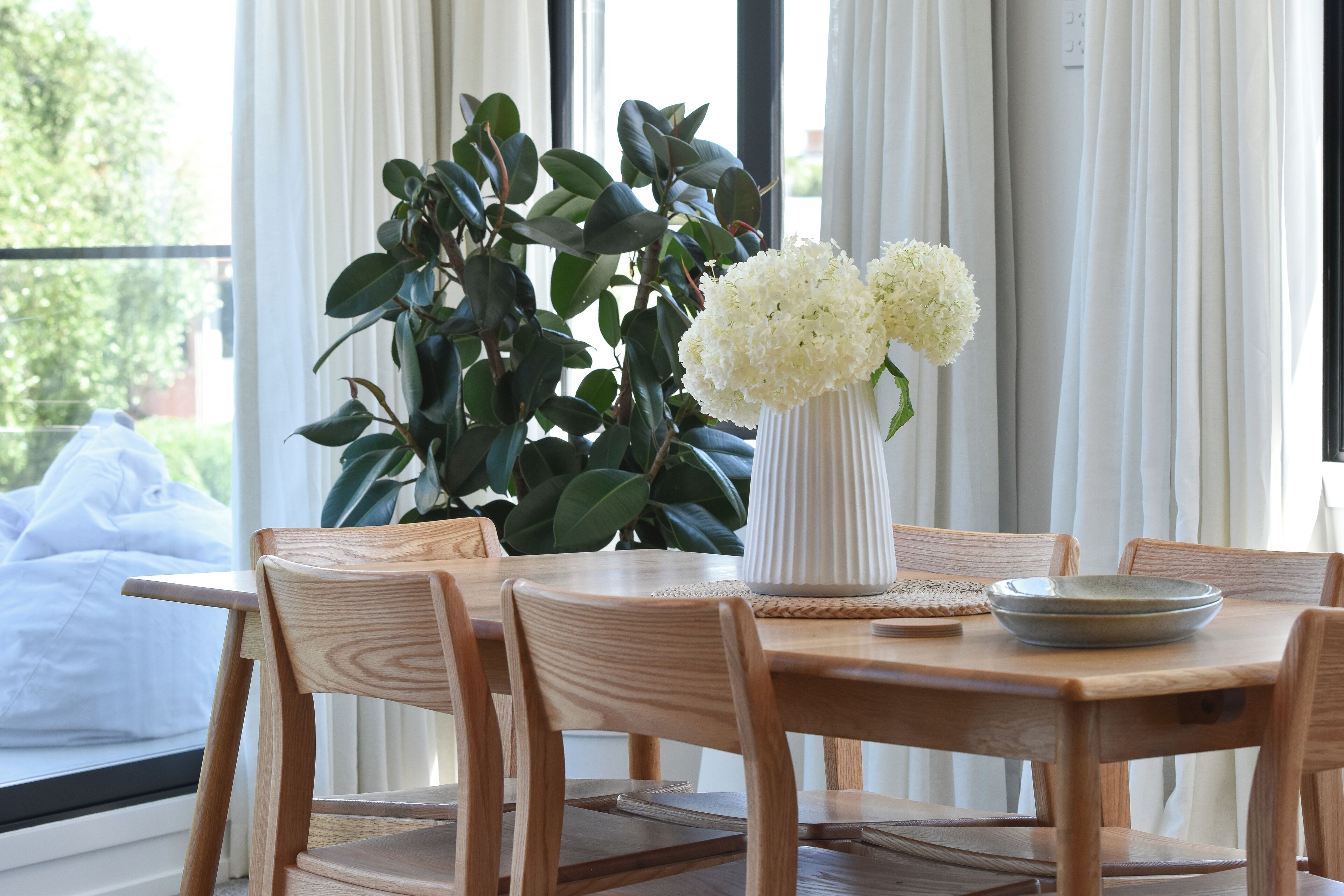 Een houten eettafel met een vaas witte bloemen, omringd door houten stoelen.