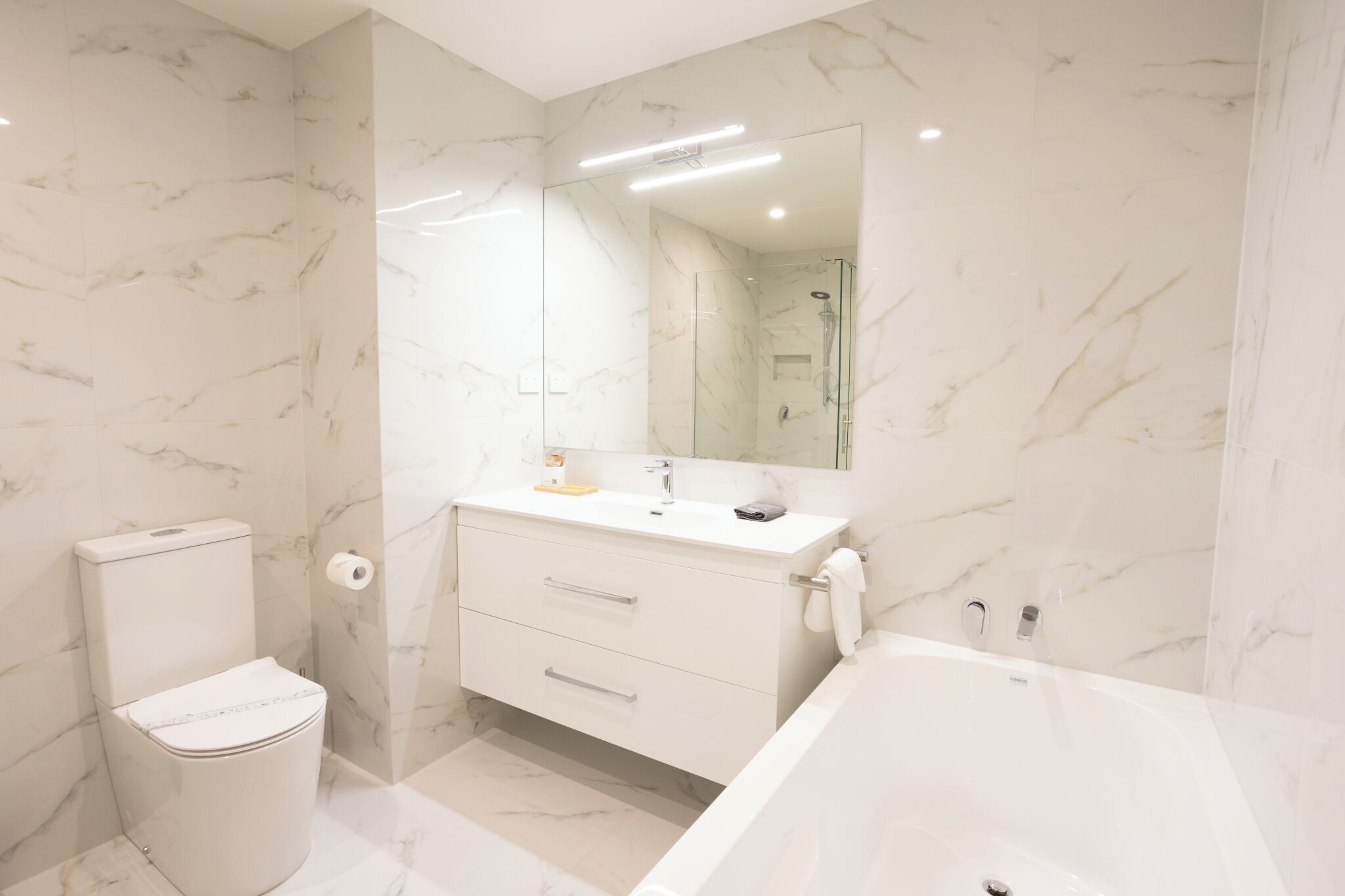 A modern bathroom with a toilet, vanity, and bathtub.