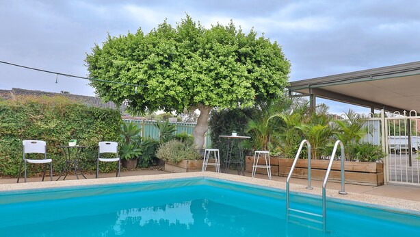 Una piscina con un árbol al fondo, rodeada de sillas y mesas.