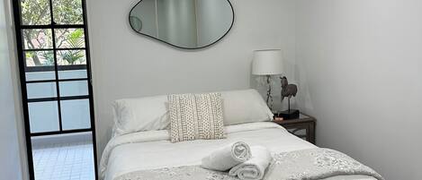 Un dormitorio con cama, lámpara de noche, espejo y vista al exterior por una puerta.