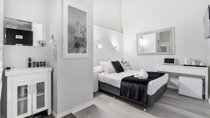 Quarto de hotel moderno com cama, mesa de cabeceira e escrivaninha com um laptop.