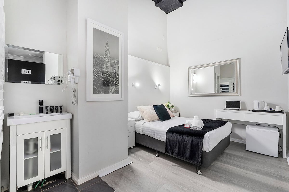 A modern hotel room with a bed, bedside table, and a desk with a laptop.