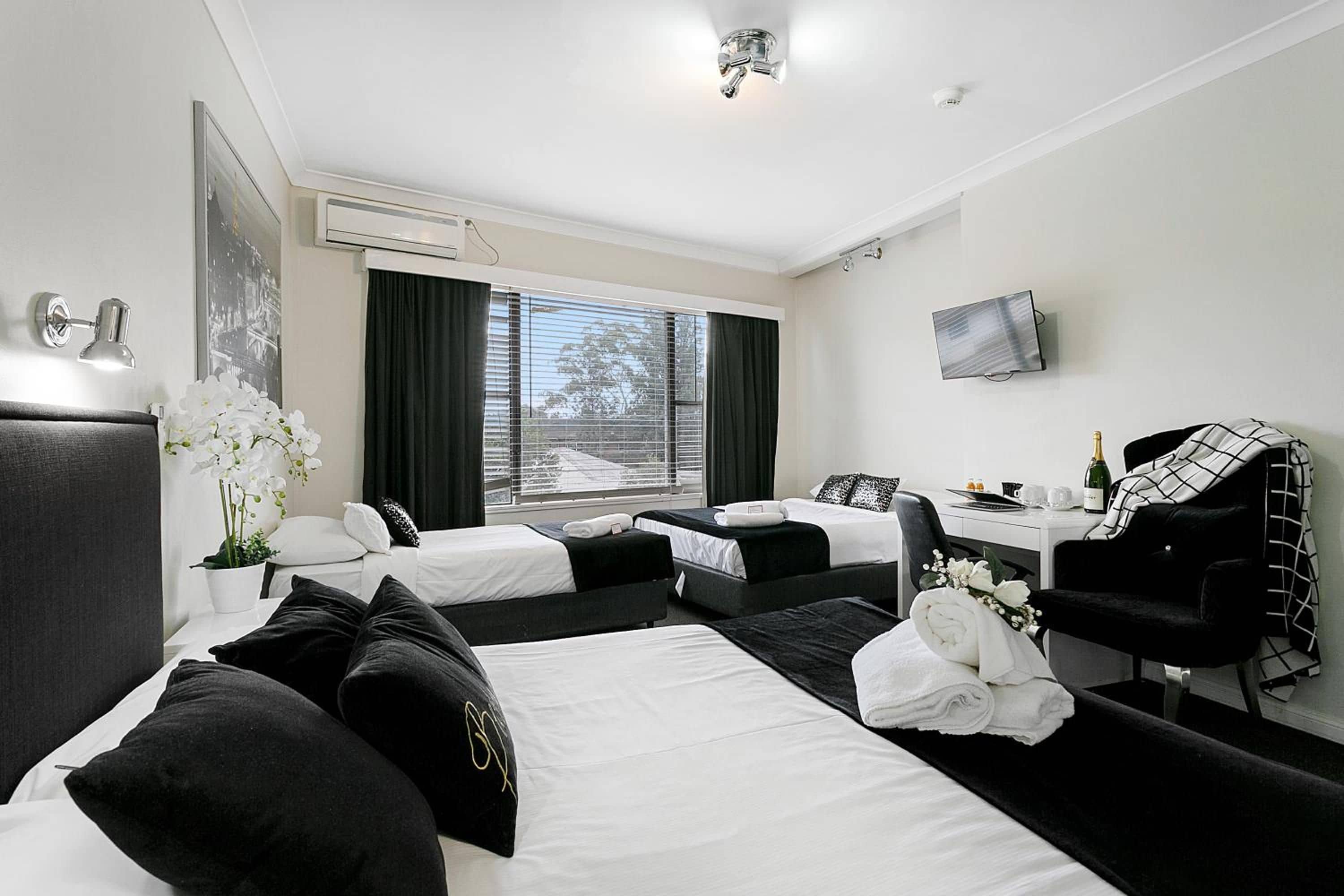 A hotel room with two beds, a desk, a chair, a television, and a window with curtains.