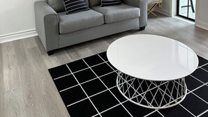 Uma sala de estar moderna com um sofá cinzento, duas obras de arte emolduradas, uma mesa de centro branca e um tapete preto e branco.