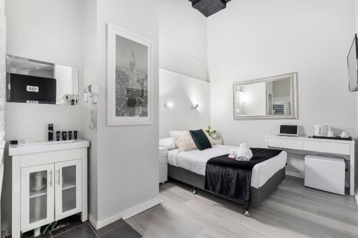 A modern hotel room with a bed, a desk, a mirror, and a cabinet.