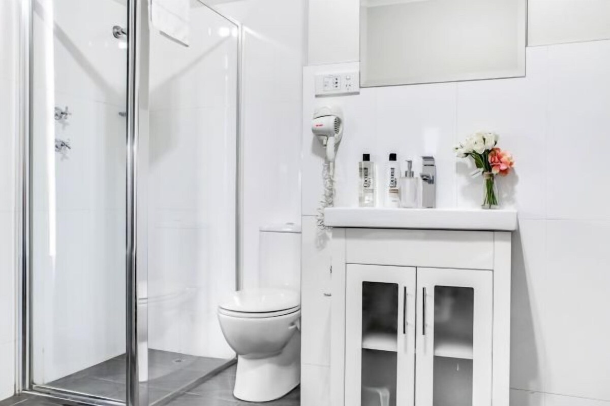 Une salle de bain moderne avec une douche à parois de verre, des toilettes blanches et un meuble-lavabo avec des placards.