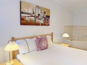 Ein Hotelzimmer mit einem Bett, zwei Nachttischlampen, einem Bild an der Wand und einer Badewanne.
