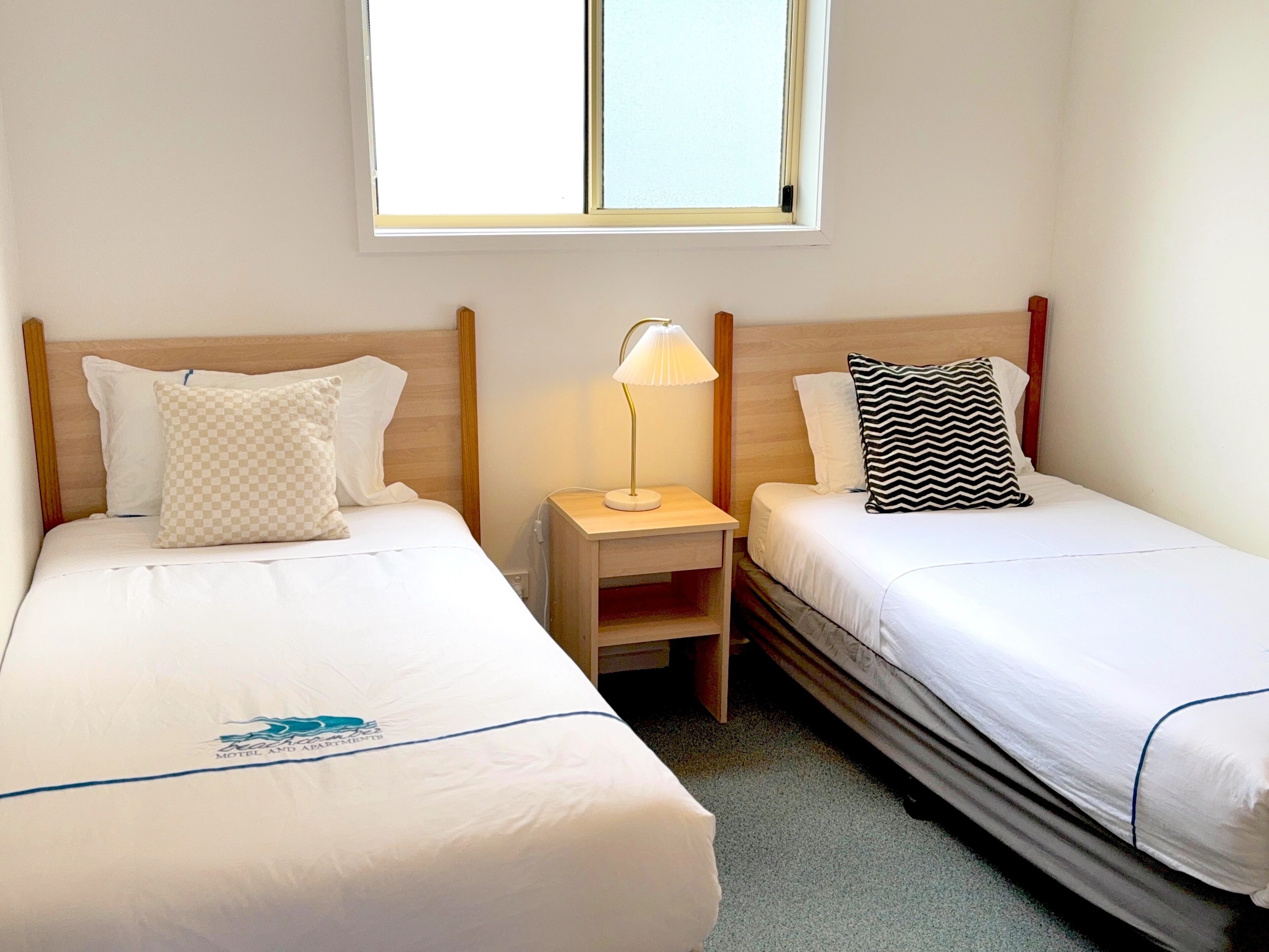 Una habitación de hotel con dos camas, cada una con una almohada y una mesita de noche con lámpara.