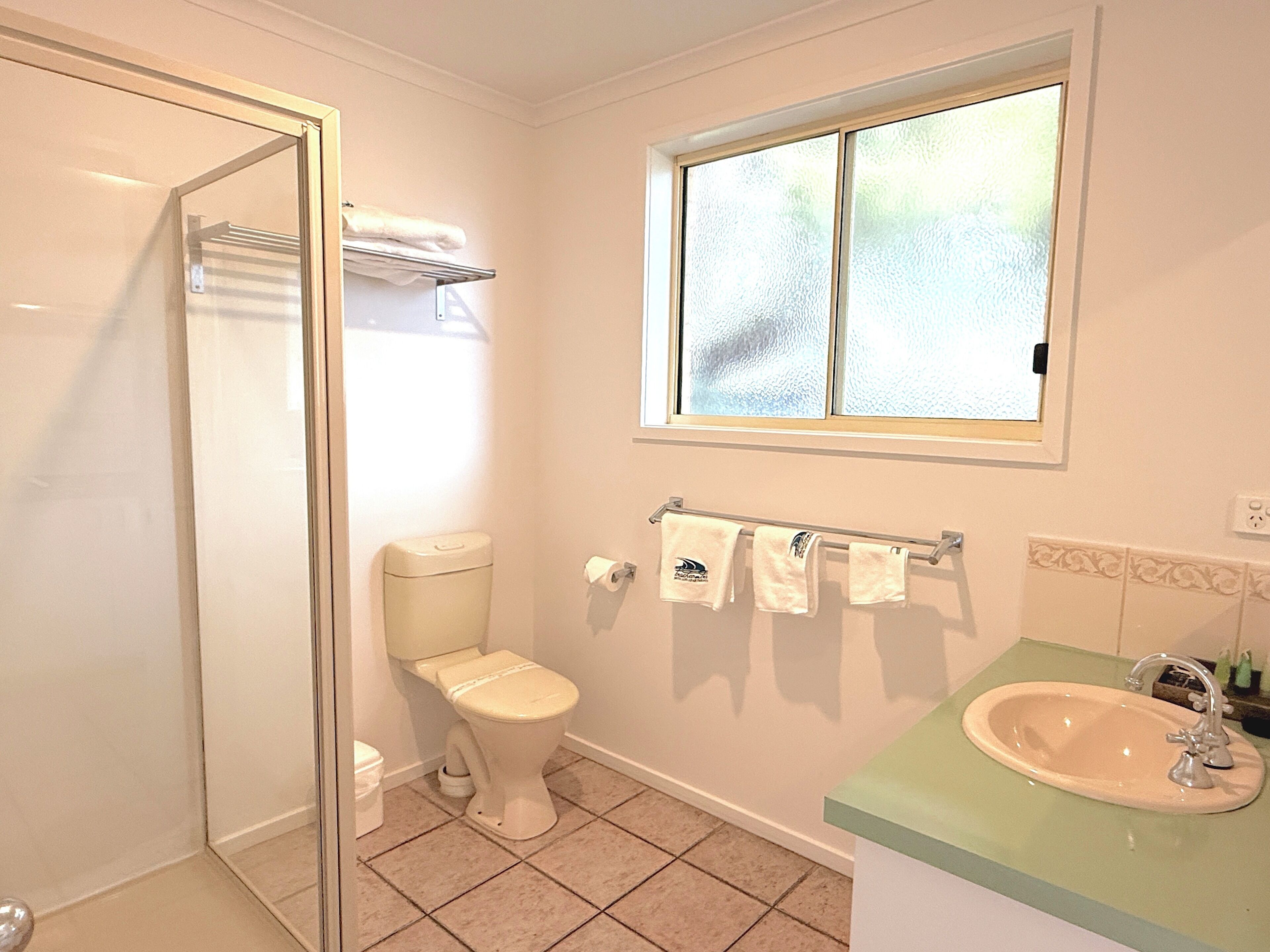 Un baño con inodoro, lavamanos, toallero y ventana.