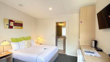 Une chambre d’hôtel avec un lit, des lampes de chevet, un bureau avec un ordinateur, un téléviseur fixé au mur et une salle de bain visible à travers une porte ouverte.