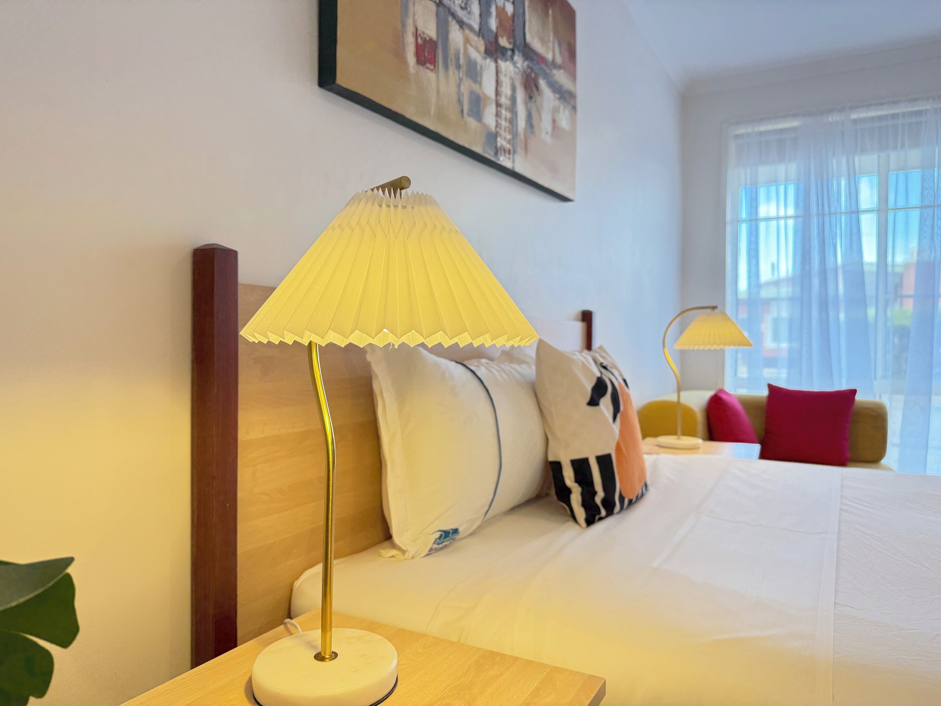 Een hotelkamer met een bed, een nachtkastje met lamp en een raam met gordijnen.