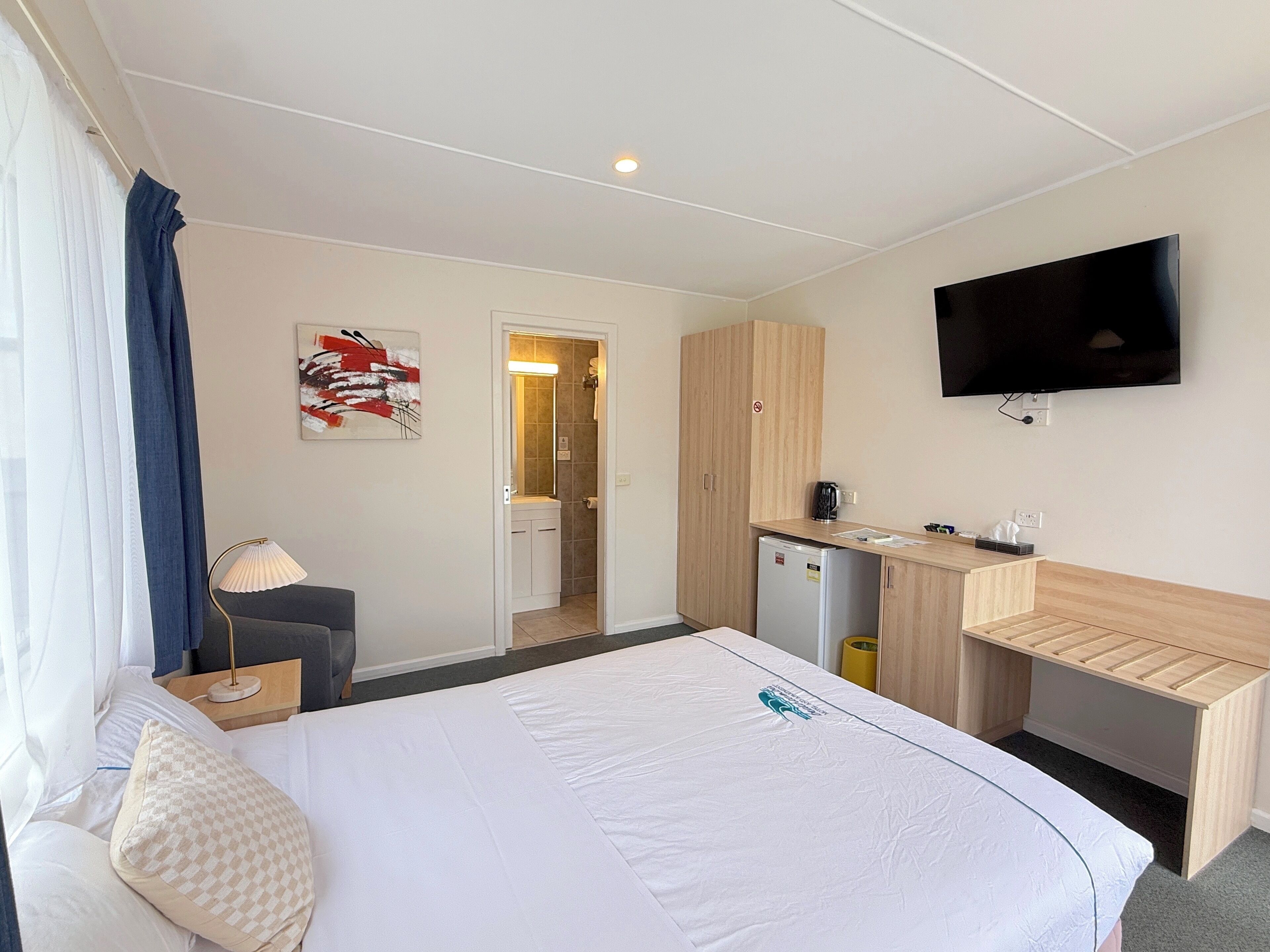 Une chambre d’hôtel comprenant un lit, un bureau, une télévision, une salle de bain et une kitchenette.