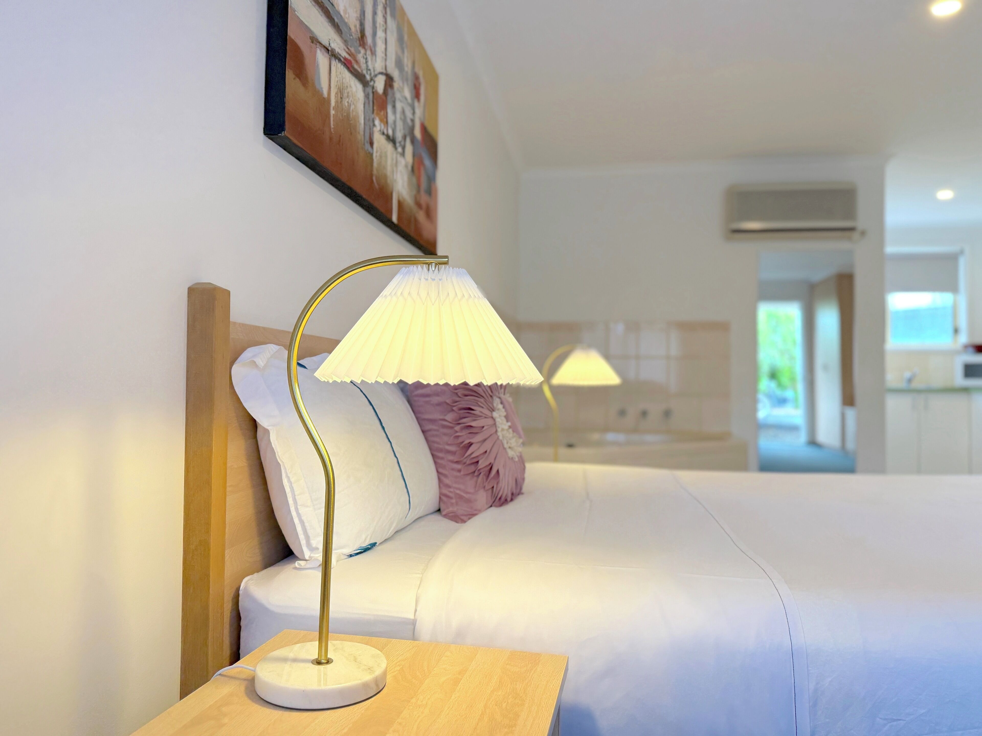 A hotel room with a bed, a bedside table with a lamp, and a painting on the wall.