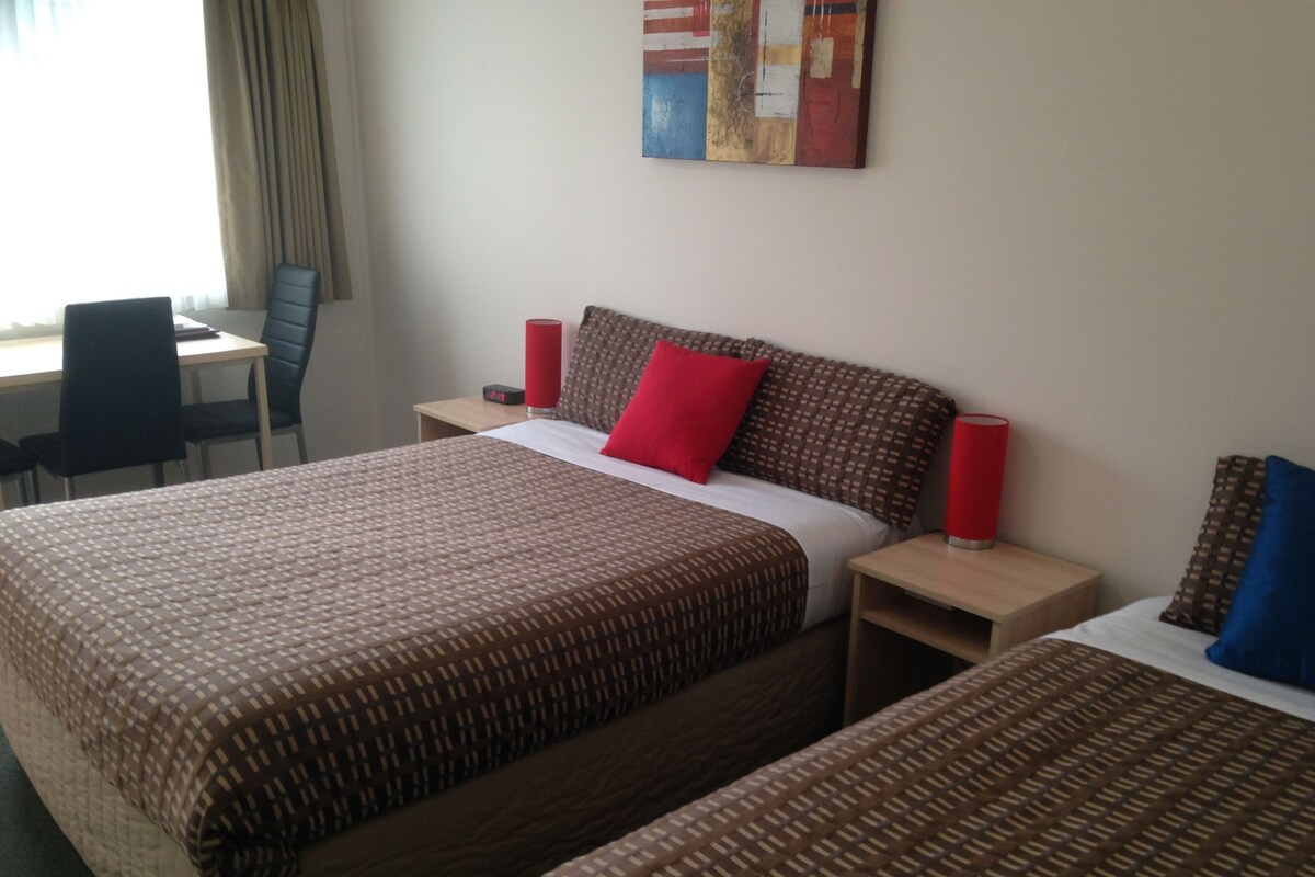 A hotel room with two beds, a desk, and a chair.