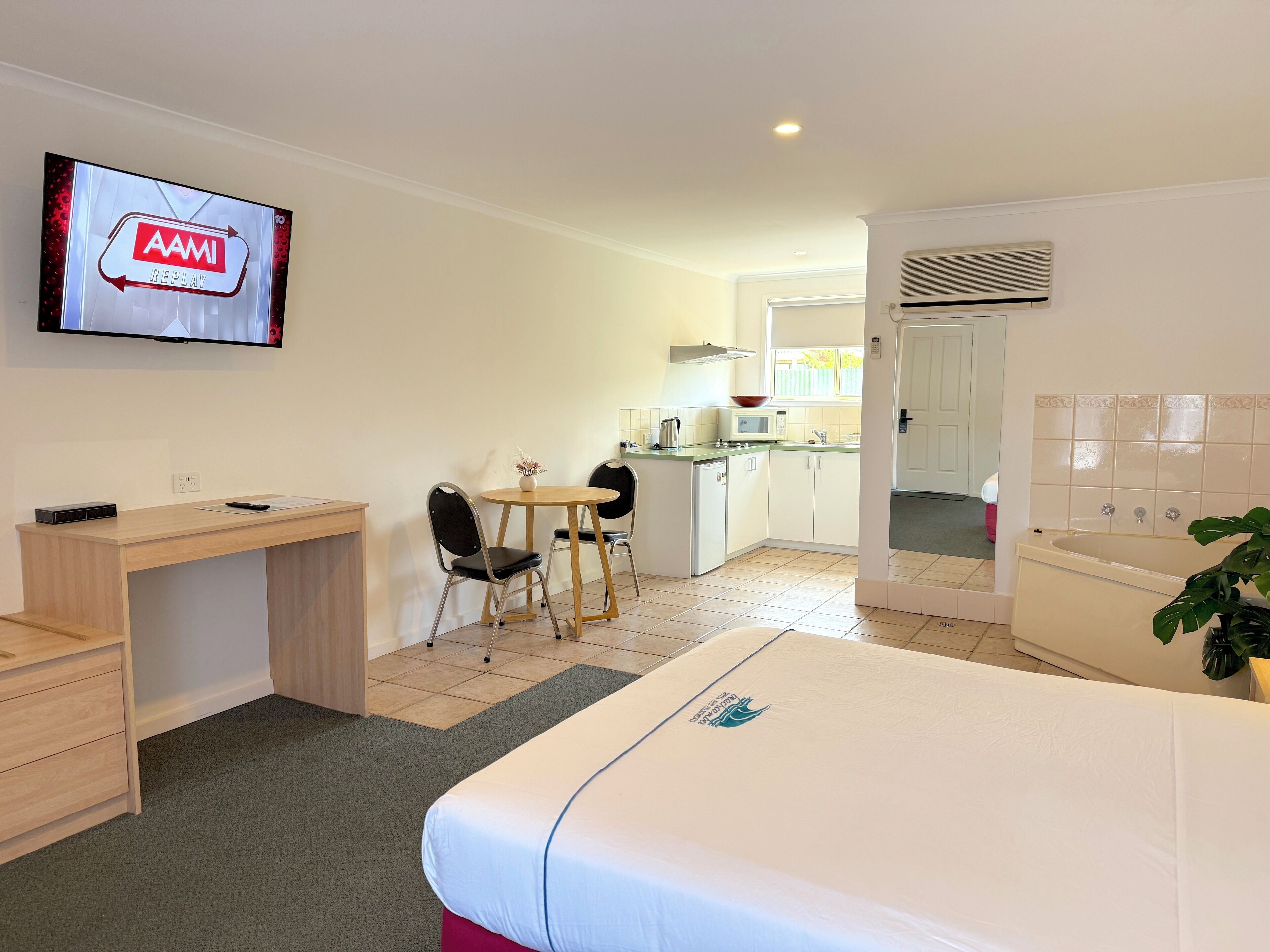 Habitación de hotel con cama, escritorio, silla, mesita, televisión, kitchenette y baño.