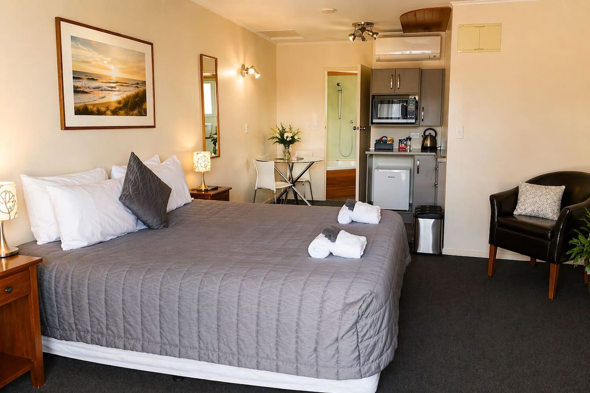 Ein Hotelzimmer mit einem großen Bett, einem Schreibtisch, einem Sessel, einer Mikrowelle und einer kleinen Küchenzeile.