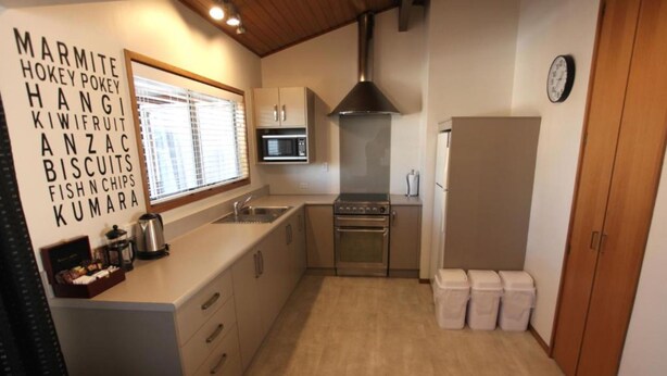 Cocina compacta con microondas, estufa y lavamanos. Hay un reloj en la pared y una ventana con persianas.