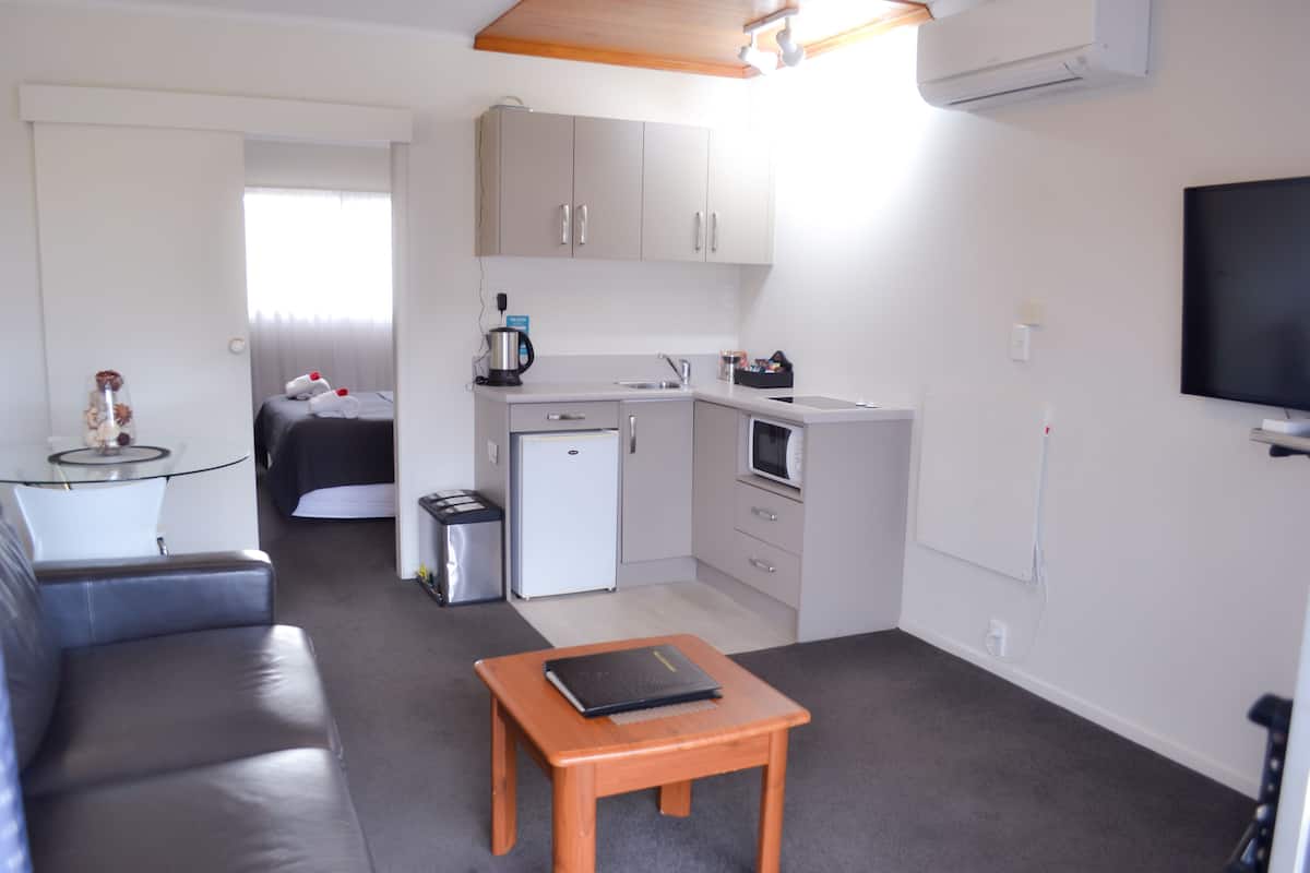 Ein kompaktes Hotelzimmer mit Küchenzeile, einem kleinen Esstisch, einer Couch und einem Fernseher.