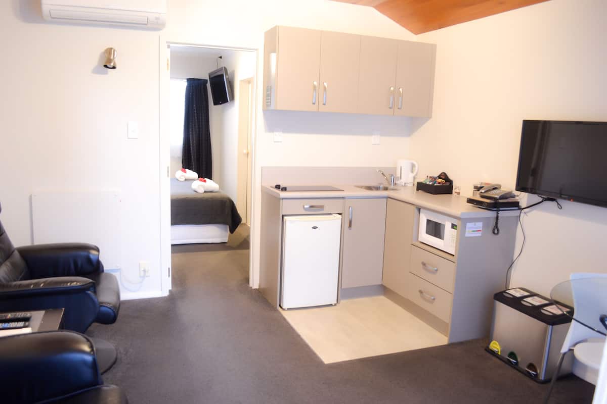 Ein kompaktes Hotelzimmer mit Küchenzeile, einer Sitzecke mit Massagesessel und einem Fernseher.
