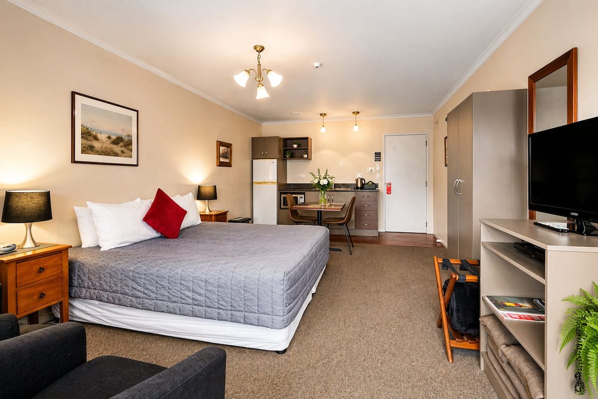 Ein Hotelzimmer mit Bett, Nachttischen, Schreibtisch, Fernseher und einer Küchenzeile.