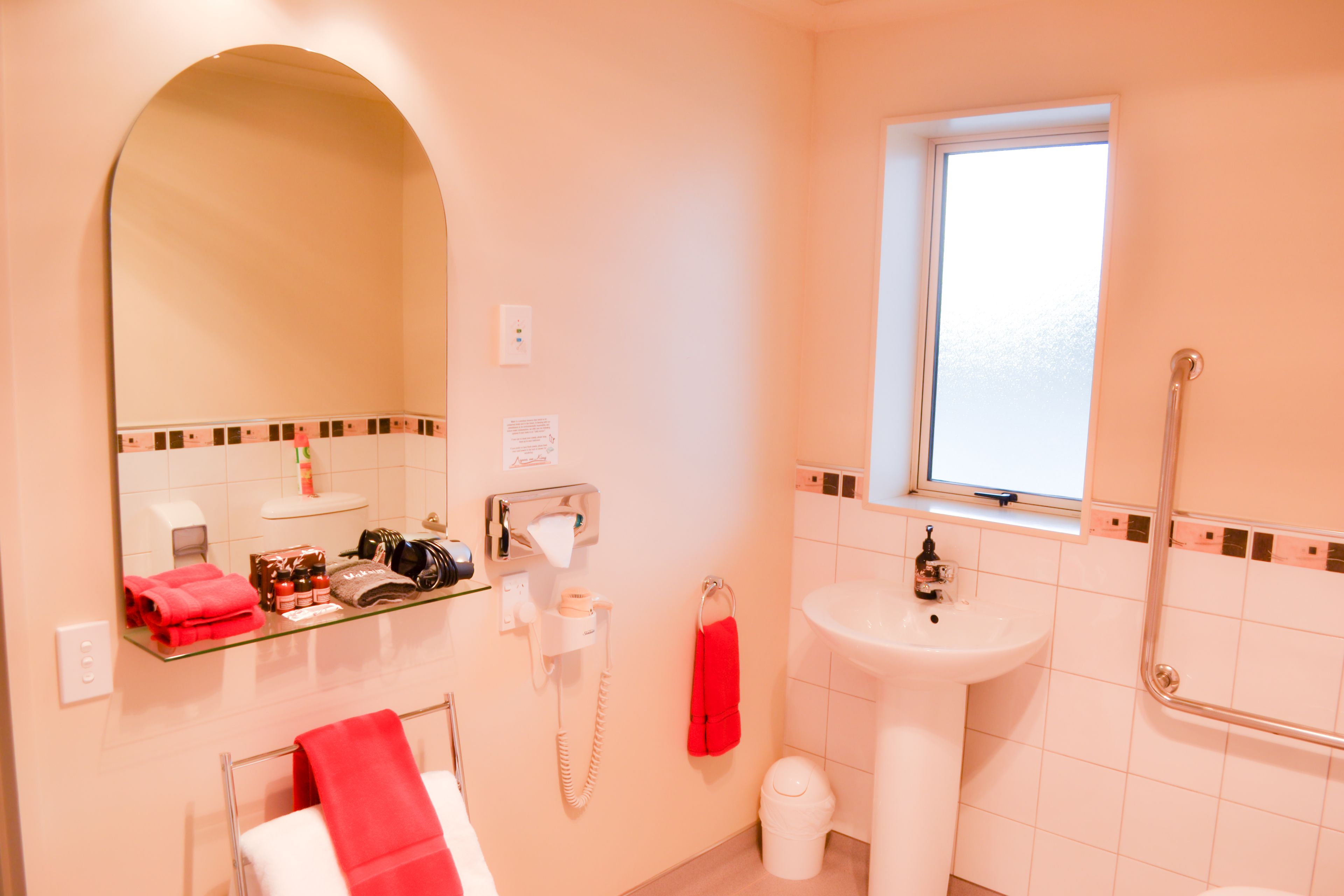 Un baño con mostrador de vidrio, lavamanos, espejo, ventana y barandilla.