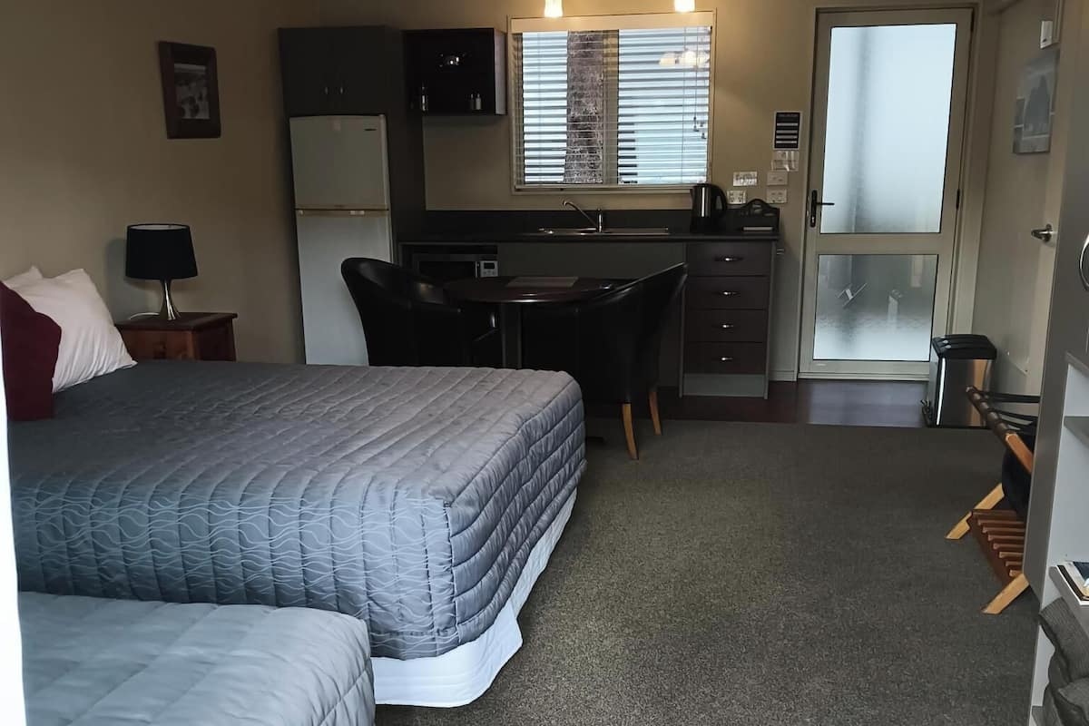 Ein kleines Zimmer mit zwei Betten, einer Küchenzeile, einem Schreibtisch und einer kleinen Sitzecke.