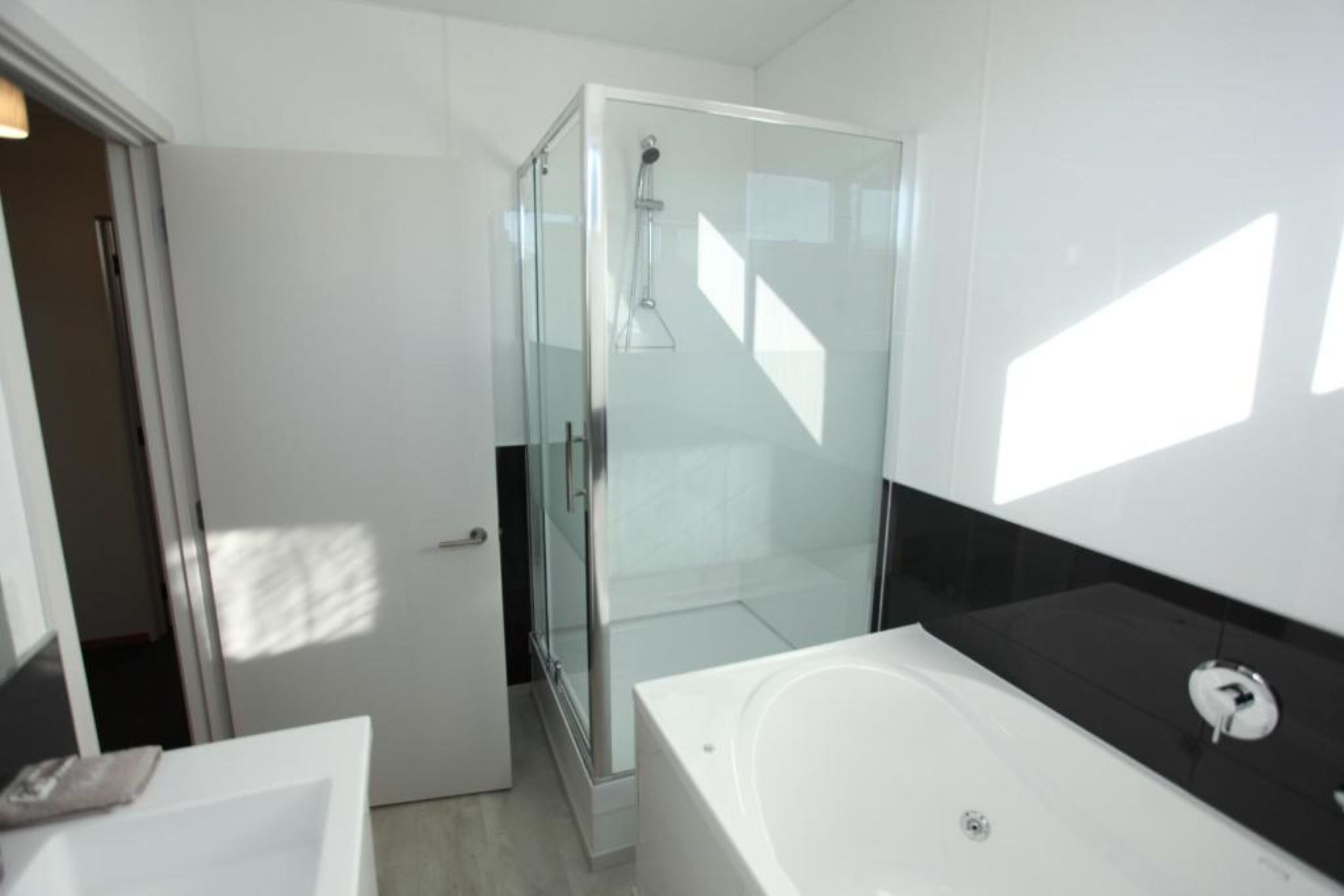 A modern bathroom with a glass-enclosed shower, a white bathtub, and a black countertop.