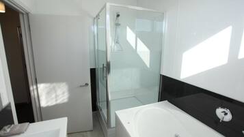A modern bathroom with a glass-enclosed shower, a white bathtub, and a black countertop.