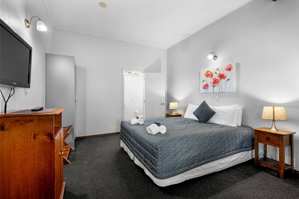 Ein Hotelzimmer mit einem Bett, einem Schreibtisch mit Fernseher, einer Lampe und einem Bild an der Wand.