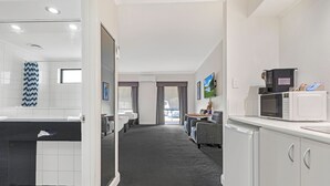 A modern hotel room with a bathroom, a kitchenette, and a view of the street. - Caledonian Hotel Motel (Echuca)
