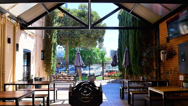 An outdoor patio area with tables and chairs, a grill, and umbrellas. - Caledonian Hotel Motel (Echuca)