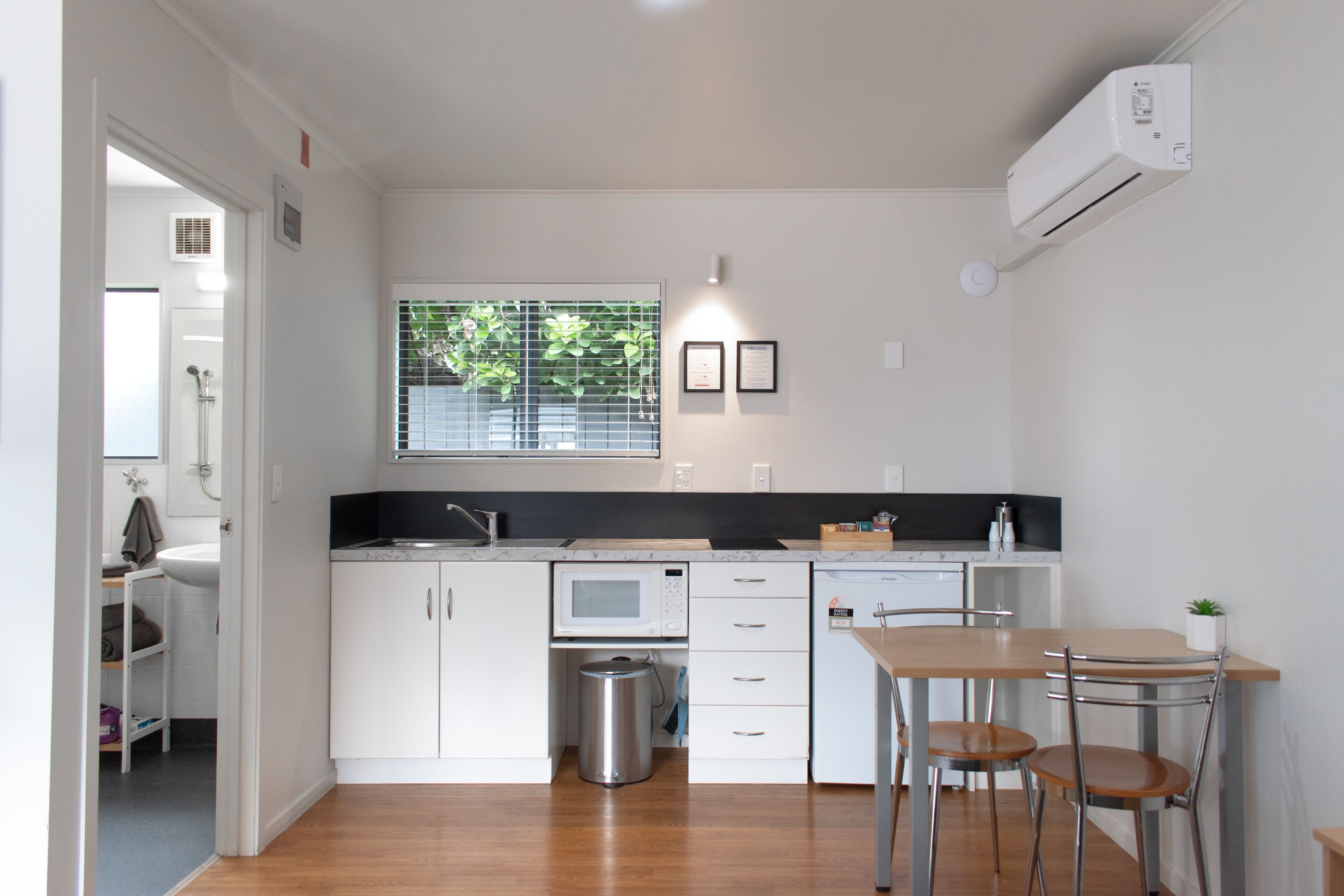 Una cocina moderna con armarios blancos, un microondas, un fregadero y una ventana con persianas.