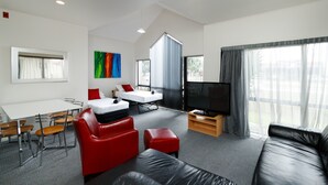 A modern living room with a sofa, red chairs, a TV, and a dining area with a table and chairs. - Drovers Motor Inn (Palmerston North)