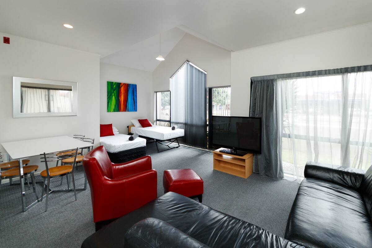 A modern living room with a sofa, red chairs, a TV, and a dining area with a table and chairs.