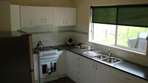 A kitchen with white cabinets, a stove, a sink, and a window with a view of greenery. - Halls on Falls Homestead (Strath Creek)