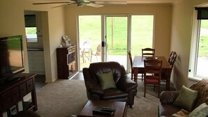 A living room with a leather sofa, a coffee table, a TV stand, and a dining area with a table and chairs. - Halls on Falls Homestead (Strath Creek)